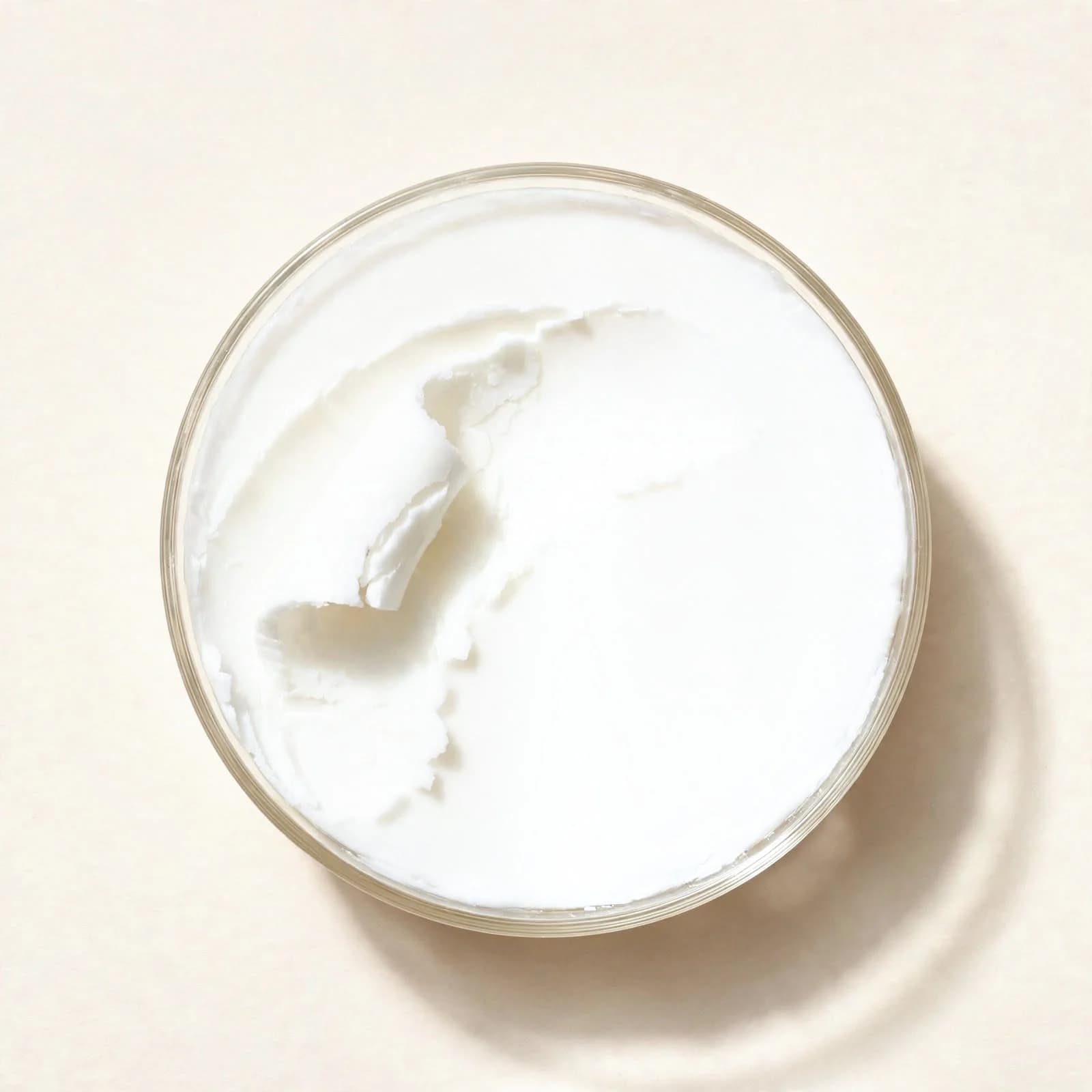 Solid white coconut oil in a glass dish, seen from above.