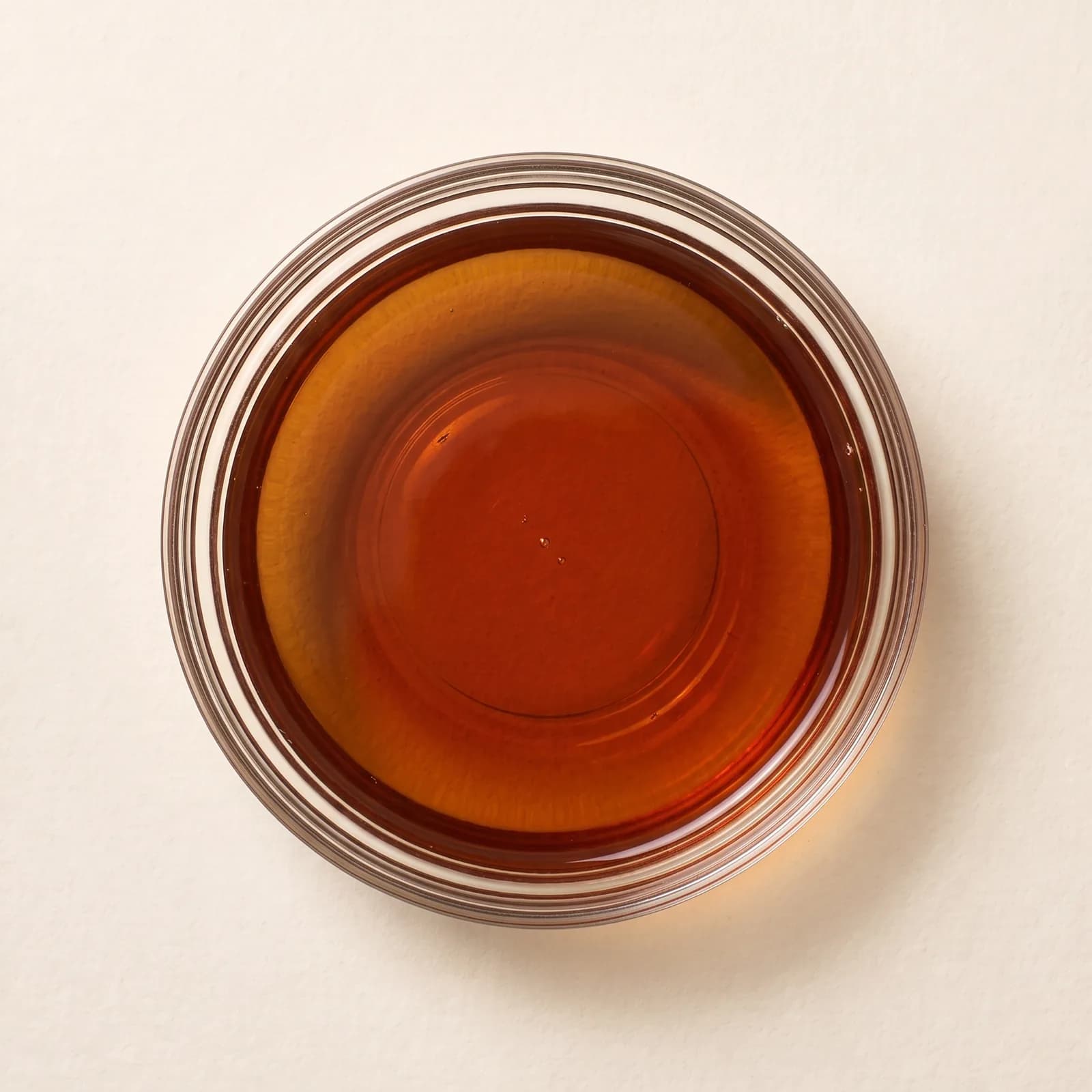 Clear amber fish sauce in a glass bowl, seen from above, the bottom of the bowl visible through it.