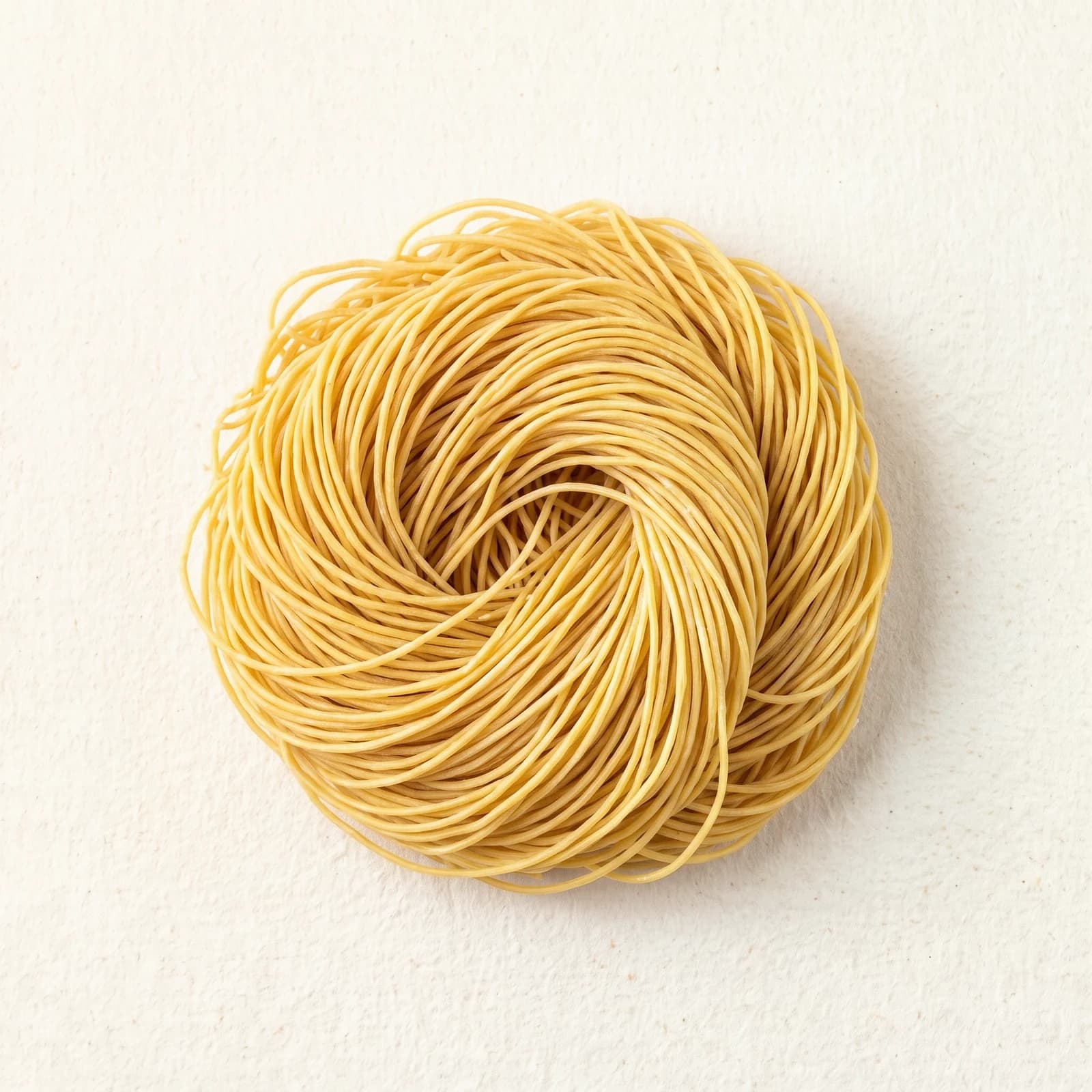 Dry lo mein noodles in a nest, showing the flat wide cut and the even color of the strand.