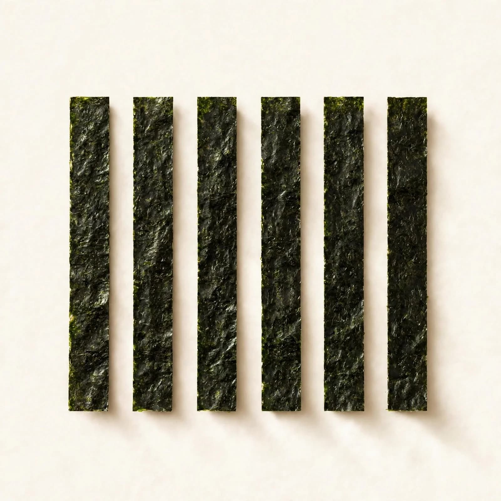 Six long strips of toasted nori cut for onigiri and handrolls, laid in a row, seen from above.