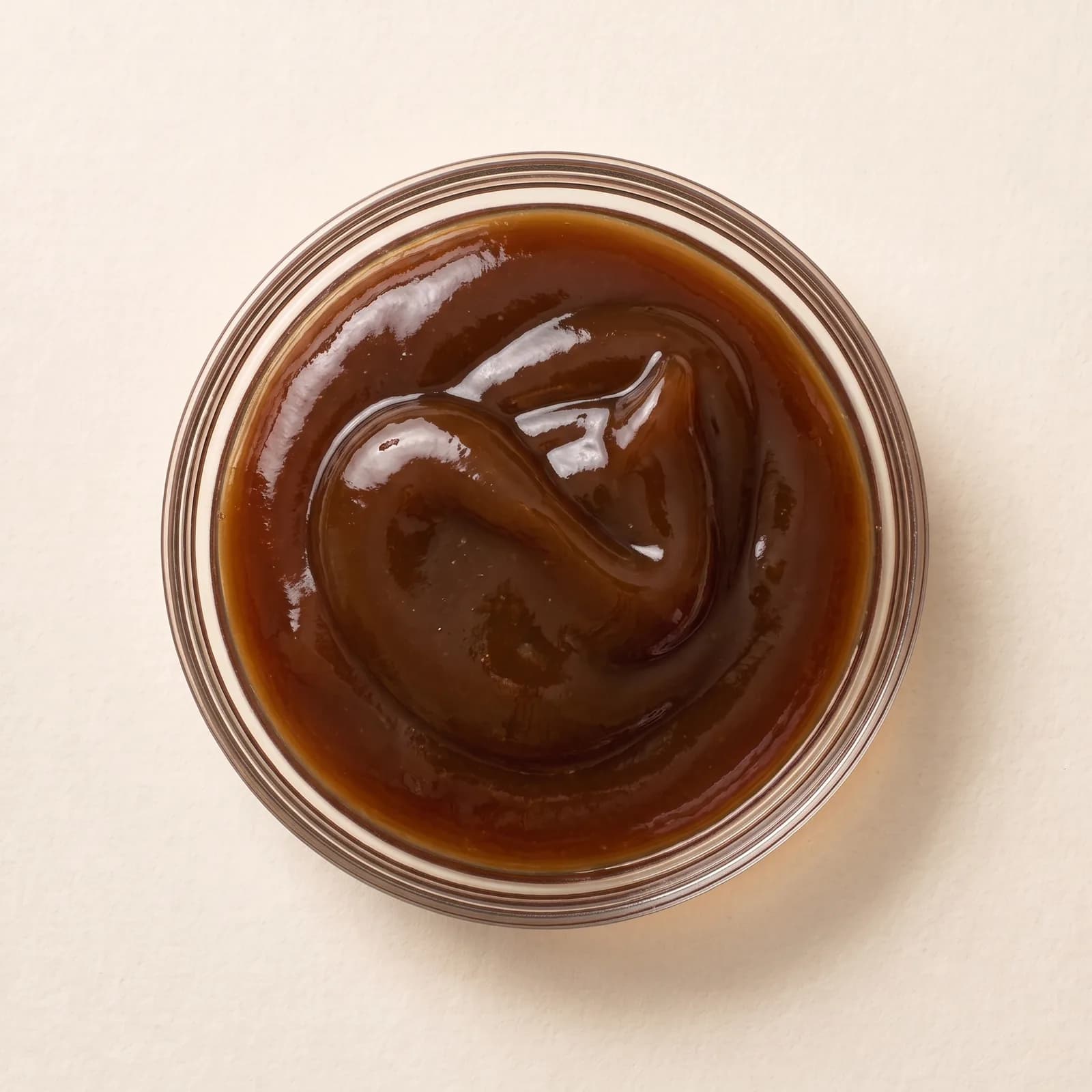 Thick, glossy oyster sauce in a clear glass bowl, seen from above, folded on the surface.