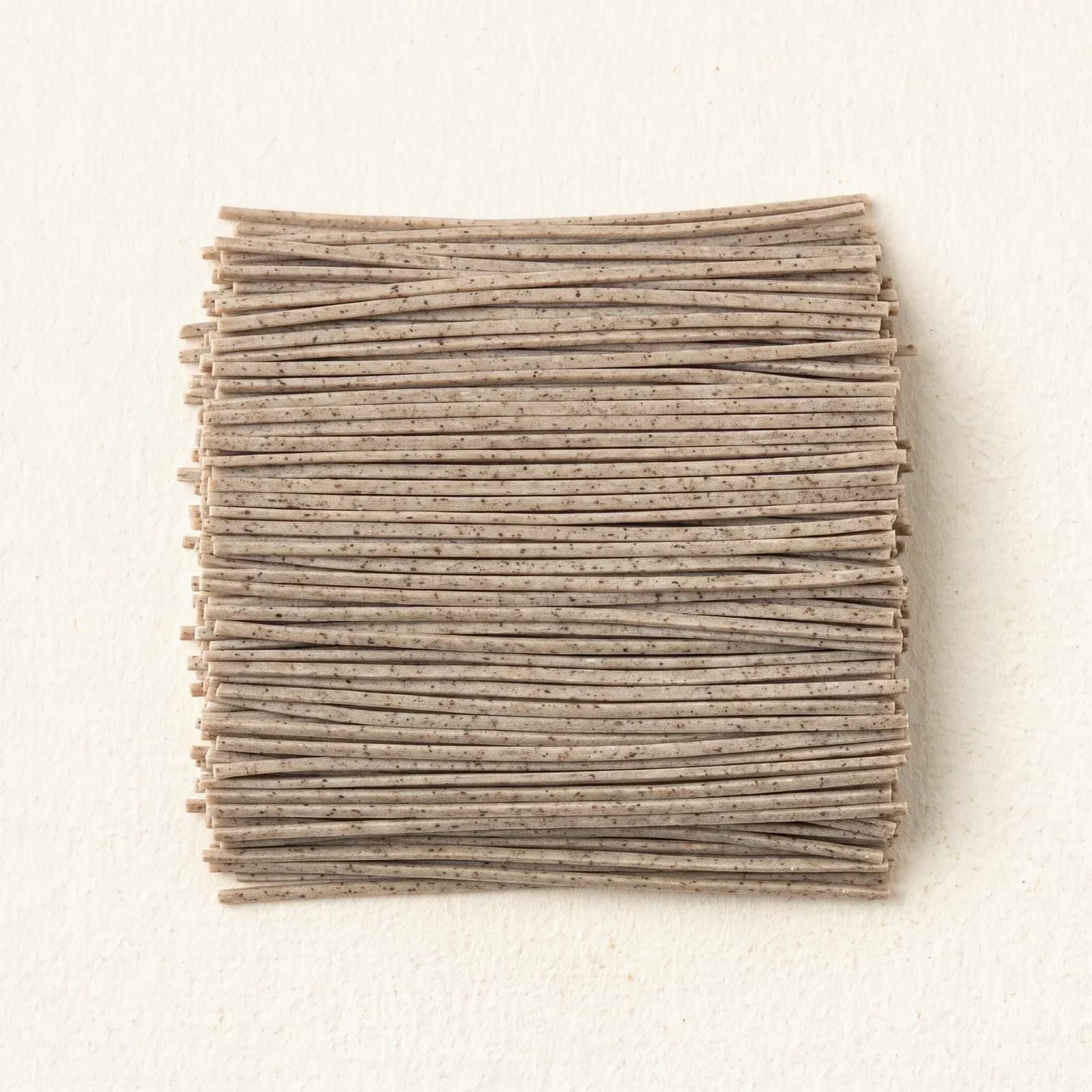 A flat bundle of dry soba noodles, showing the straight narrow cut and the dark buckwheat flecks in the strand.