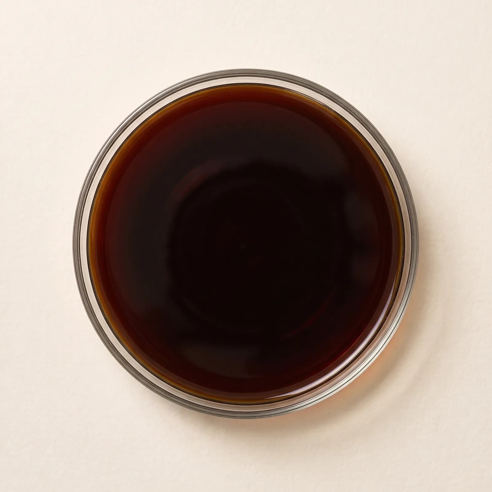 Tamari in a clear glass bowl, seen from above, almost black at the center and red-brown at the edge.