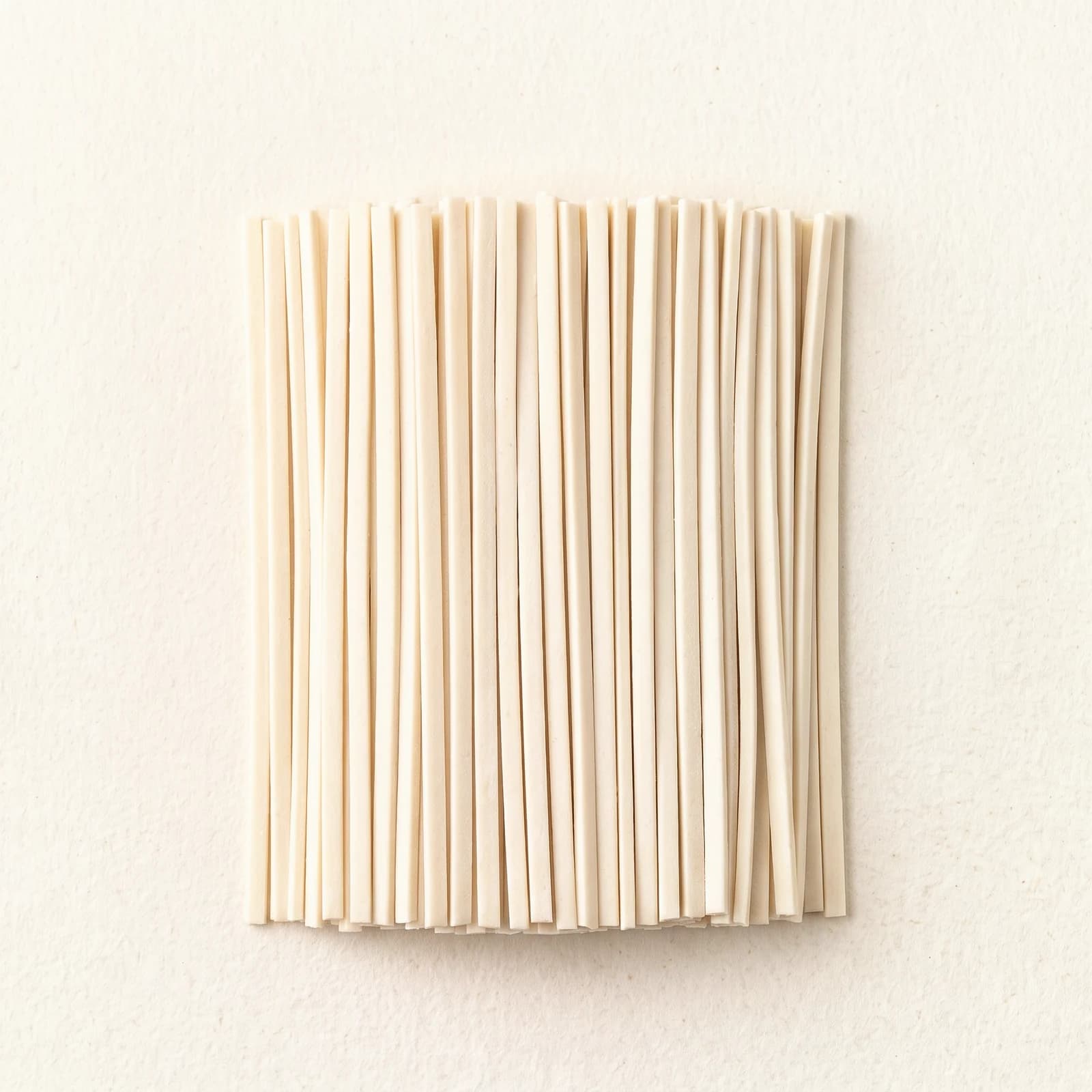 Straight lengths of dry udon noodles, showing the thick square cut and the off-white surface.