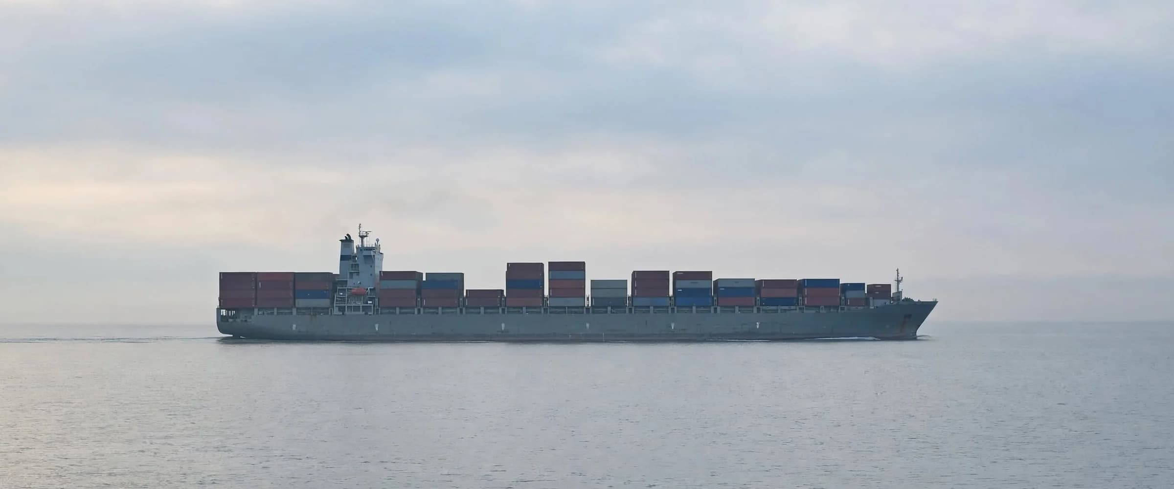 A loaded container ship at sea under an overcast sky.